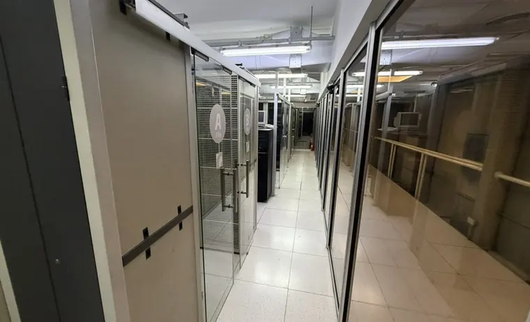Corredor entre jaulas privadas de gabinetes, con puertas vidriadas identificadas por fila